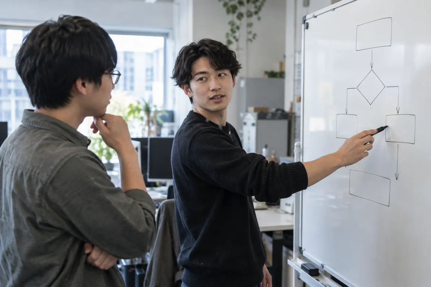Two young colleagues discussing an unlabelled physical process diagram in an operations office