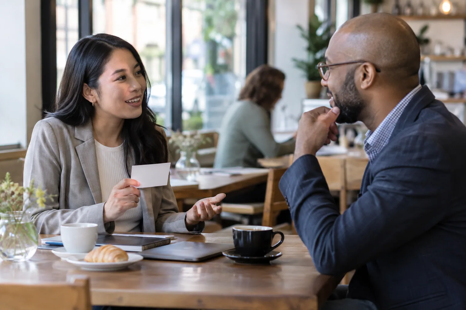 Two professionals discussing a reference request face to face in a daytime cafe